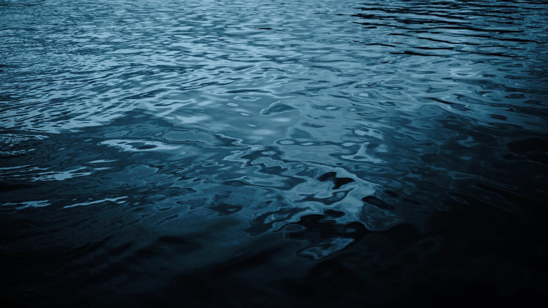 Black blue water background with reflection of light waves ripples dark dramatic sea surface