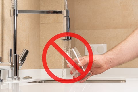 Hand fills a glass with water from the tap, accompanied by red prohibition symbol, warning of undrinkable, polluted water