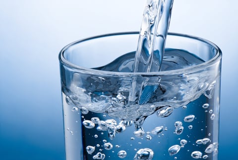 Pouring water into glass on a blue background