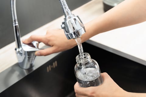 Close-up of a woman filling a glass bottle with tap water