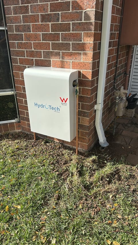 White HydroTech water system unit mounted on a red brick wall exterior