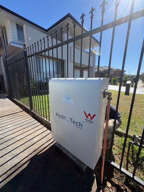 White HydraTech water tank installed outside a residential property next to a black metal fence