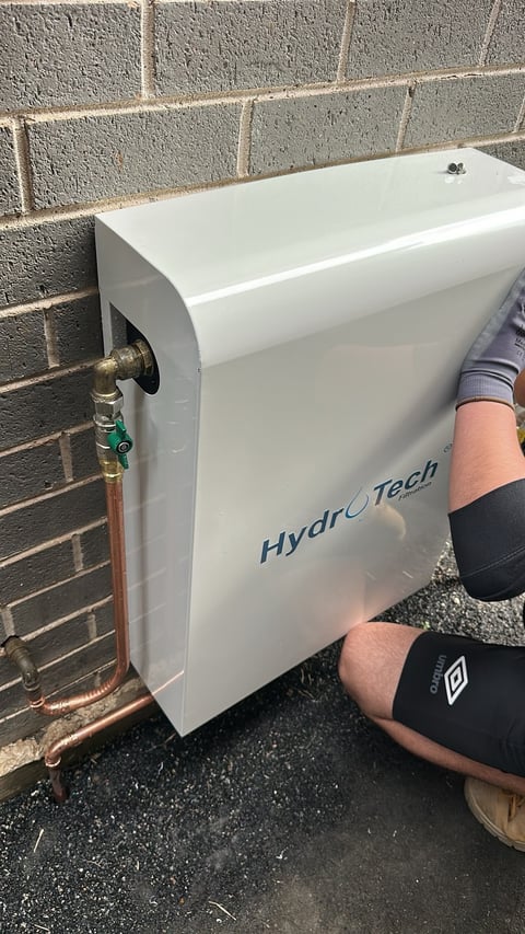 Person installing a white HydroTech water filtration system on a brick wall with copper piping connections