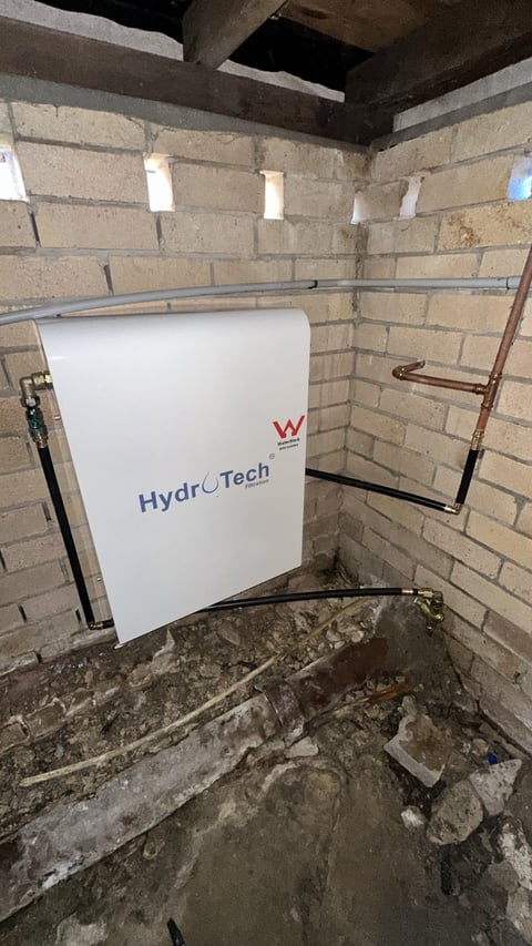 HydroTech water tank installed in brick basement under exposed concrete beams with copper piping