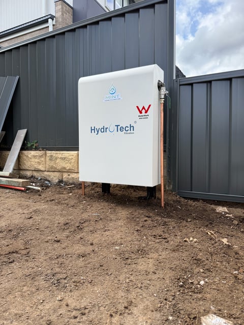 White HydroTech water tank system installed outside a gray metal building on dirt ground